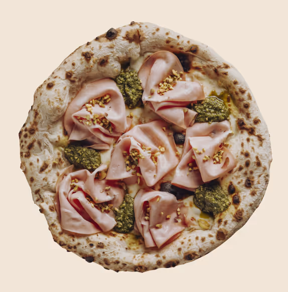 Pizza with folded slices of ham, dollops of green pesto, and sprinkled chopped nuts on a charred crust.