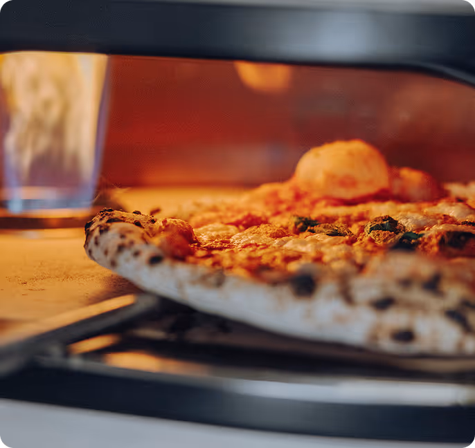 Close-up of a pizza baking inside an oven with a glass of water in the background.