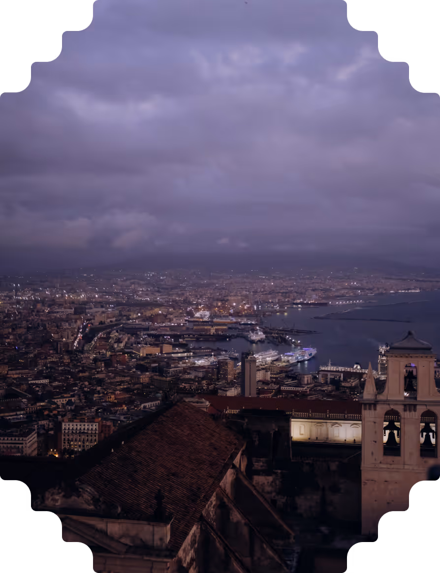 Evening cityscape with a harbor, cruise ships, and bell tower under a cloudy purple sky.