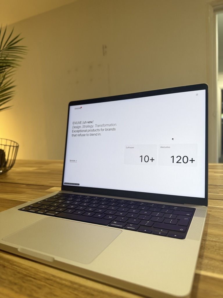 Open laptop on a wooden table displaying a website with text about design, strategy, and transformation, showing 10+ software and 120+ websites.