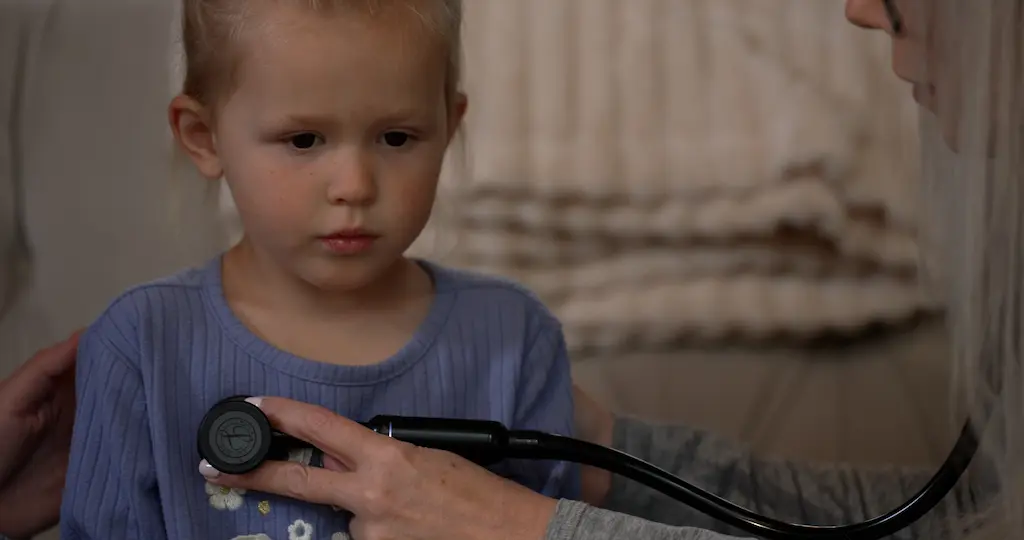 A young girl being medically evaluated with a stethoscope held to her chest.