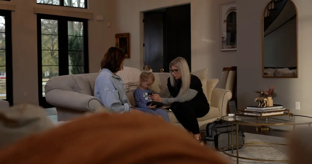 A nurse treating a mother and daughter on a couch inside a home. 