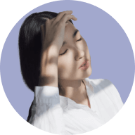 Young woman with eyes closed shading her face with hand against sunlight.