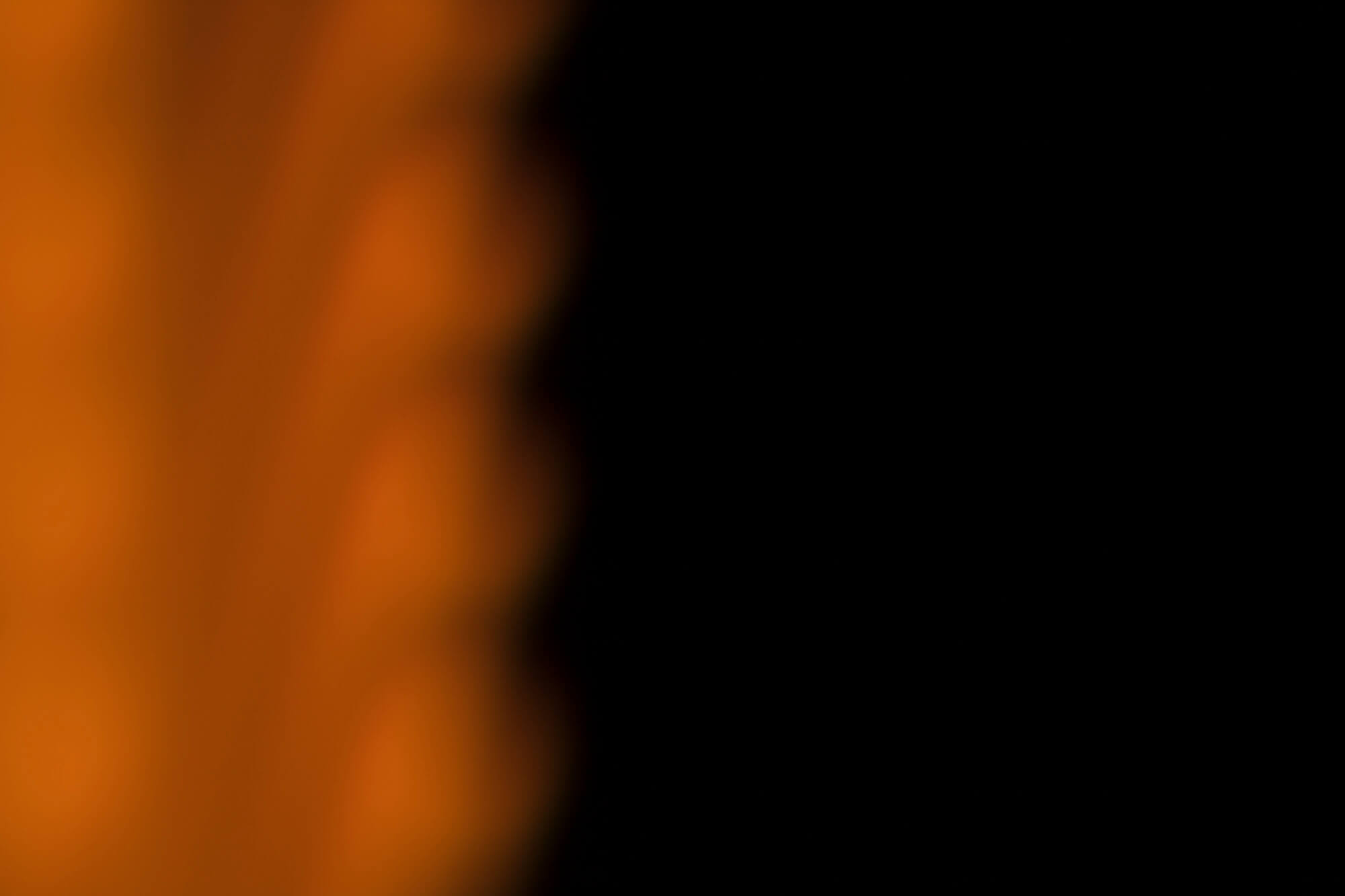 Epätarkka kuva oranssista valosta tummaa taustaa vasten, luoden abstraktin ja hämärän tunnelman.
