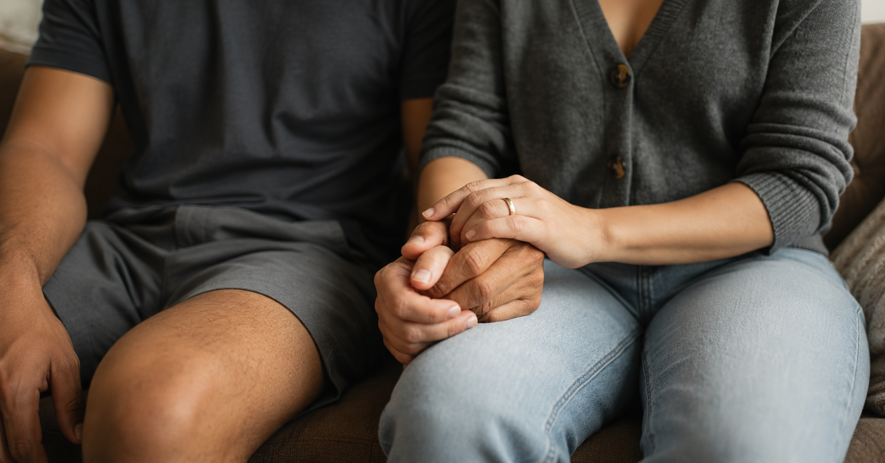 Couple holding hands while sitting together on a sofa, offering comfort and support during their fertility journey.