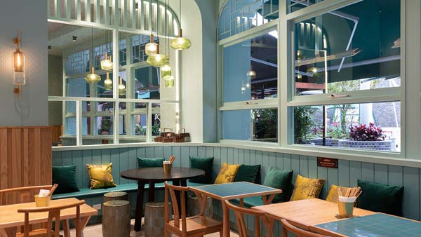 Cozy cafe interior with teal wainscoting, wooden tables and chairs, green and yellow cushions, and hanging pendant lights.