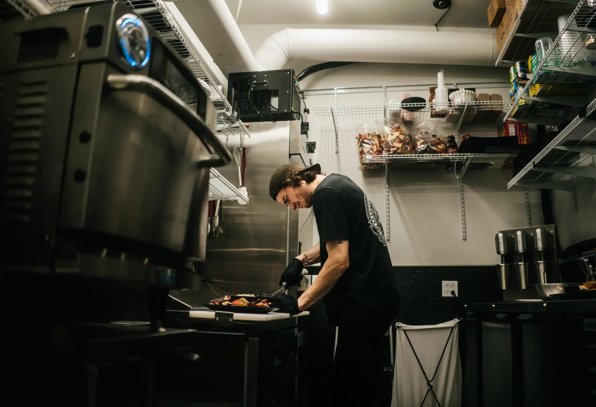 Chef preparing food on a cutting board inside a commercial kitchen surrounded by stainless steel equipment.