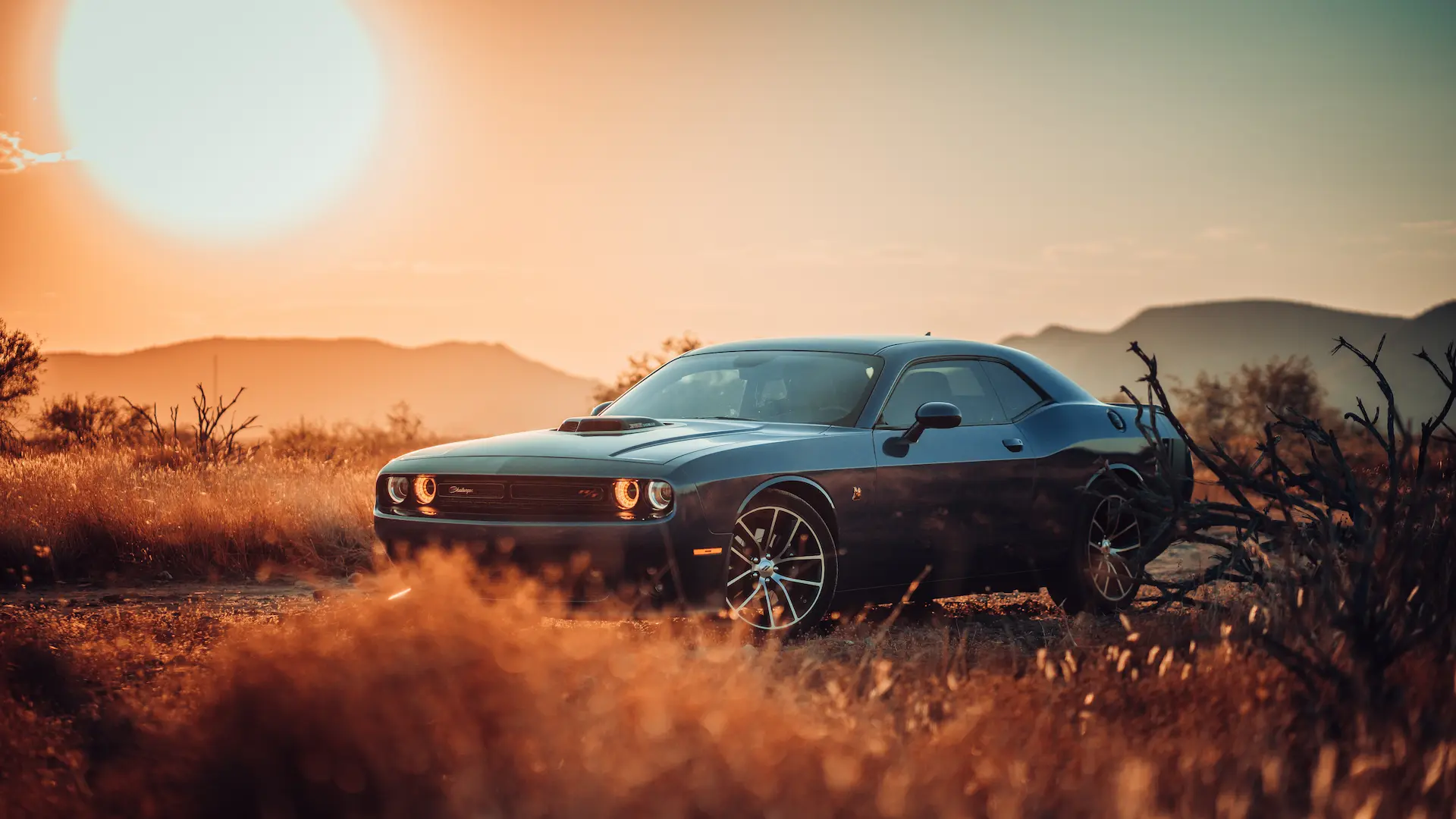 Black sports car parked in a desert landscape at sunset with mountains in the background.