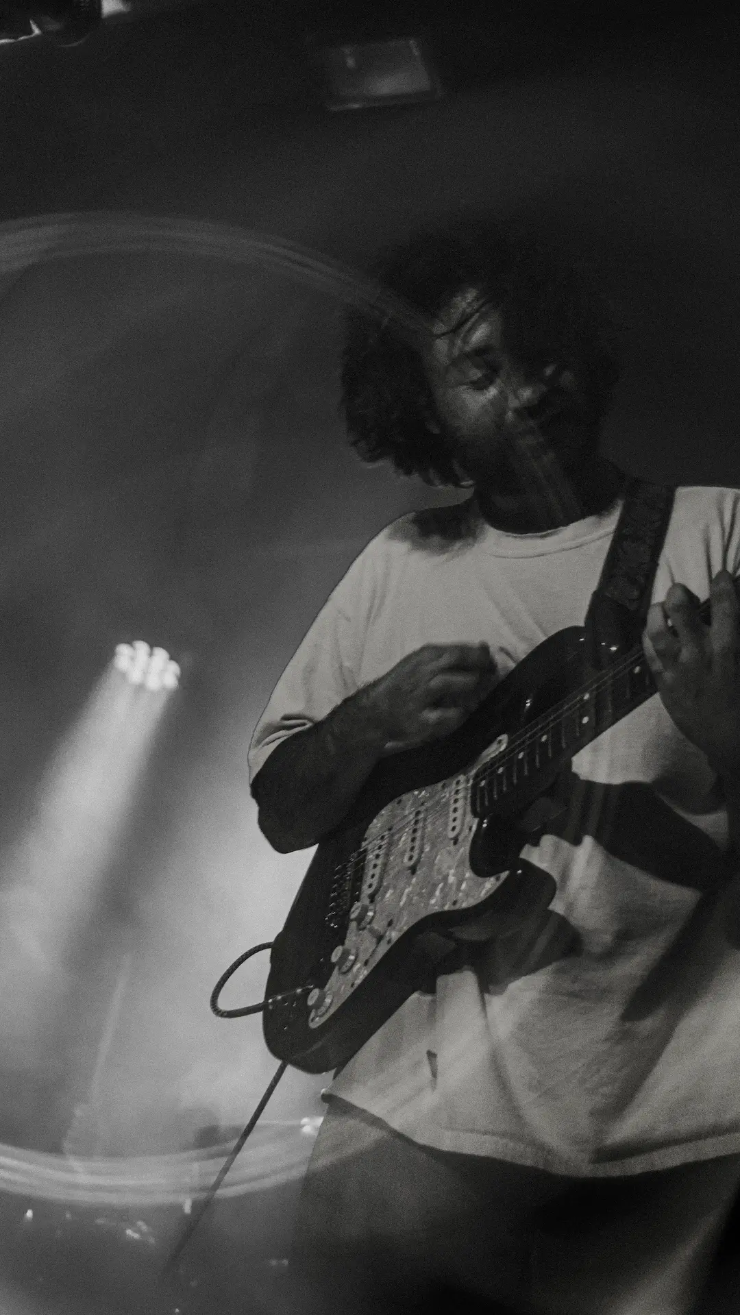 Musician playing an electric guitar on stage, captured in black and white with dramatic lighting.