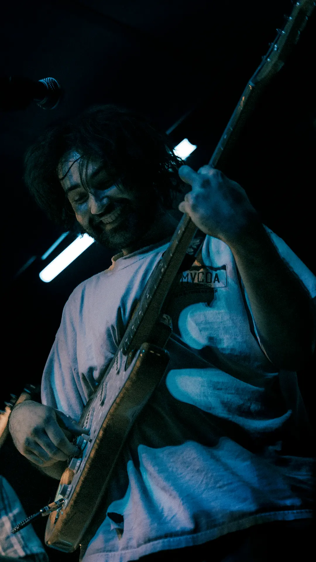 Musician playing an electric guitar on stage under blue stage lighting.