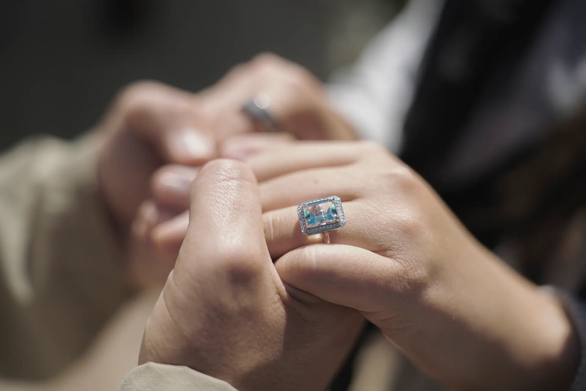 Close-up of a person placing an engagement ring on another person’s finger.