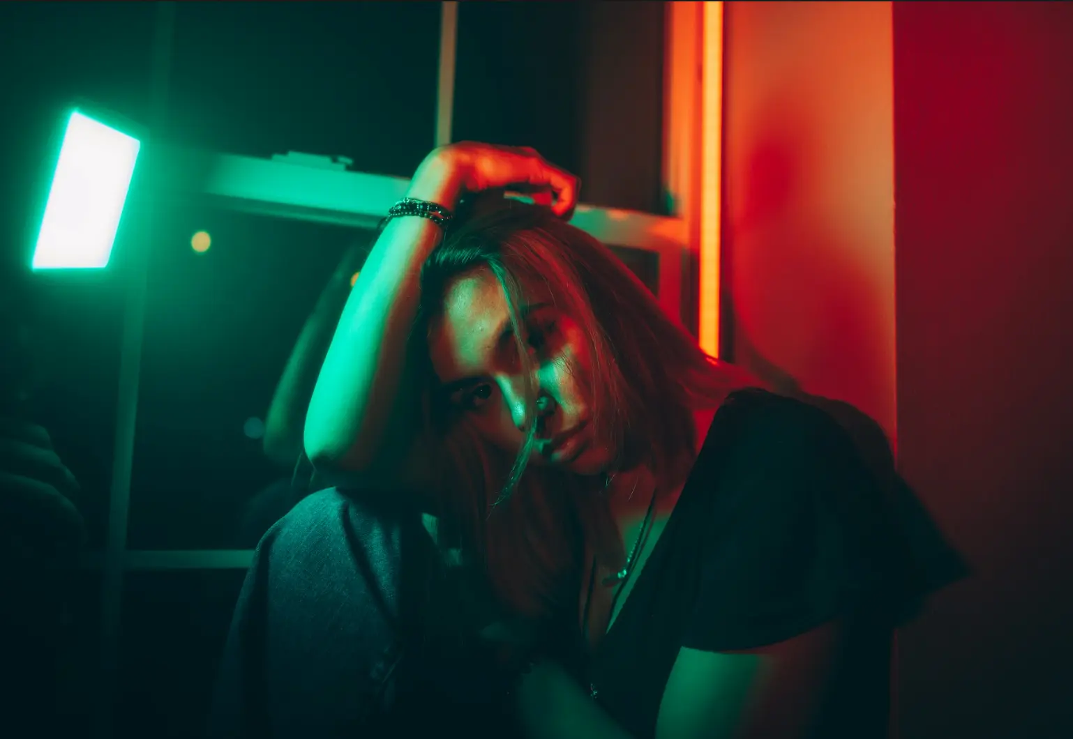 Person leaning forward indoors, lit by contrasting green and red light in a cinematic setting.