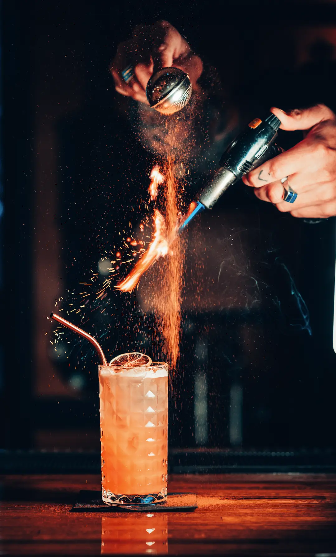 Bartender pouring a drink into a glass as liquid splashes upward on a dark bar surface.