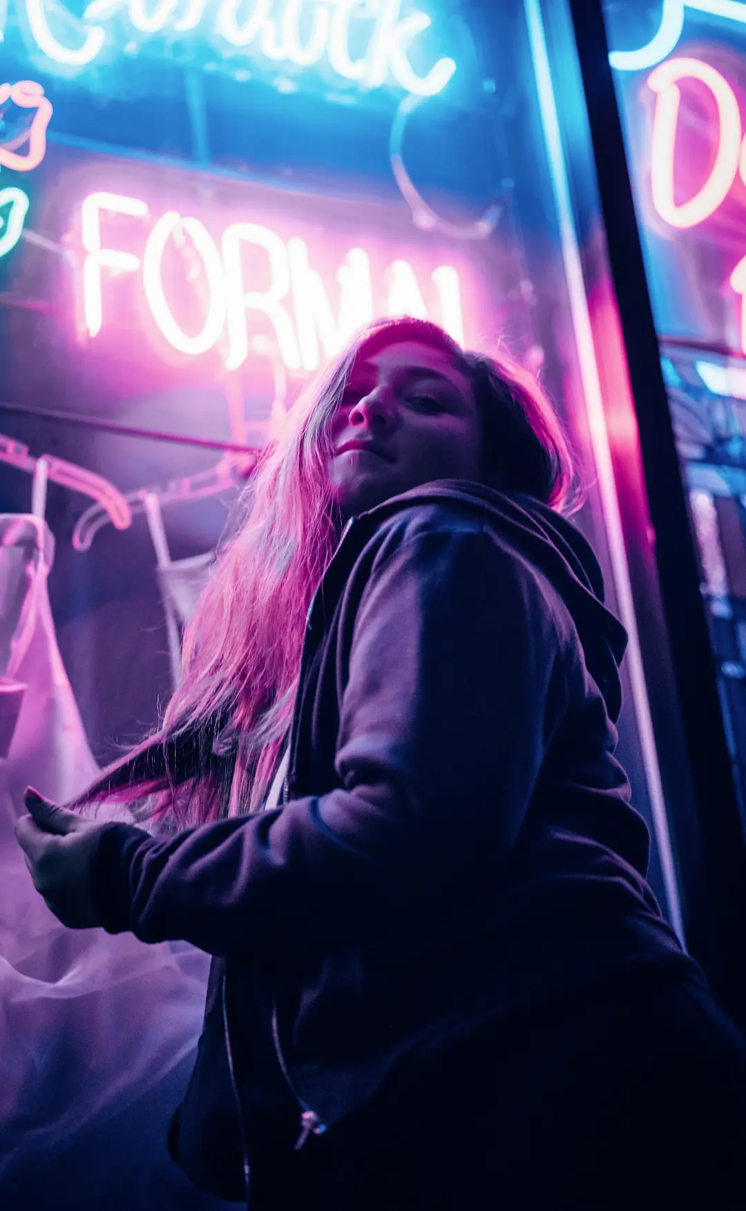 Person standing near a storefront window illuminated by pink and blue neon lights at night.