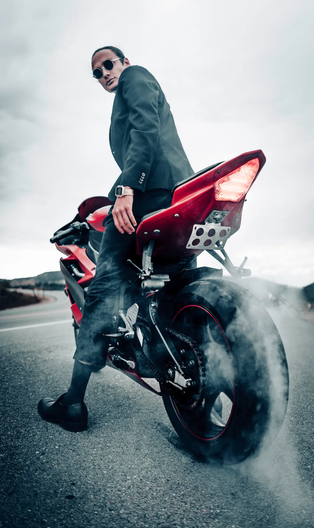 Person sitting on a red sport motorcycle as smoke rises from the rear tire on a paved road.