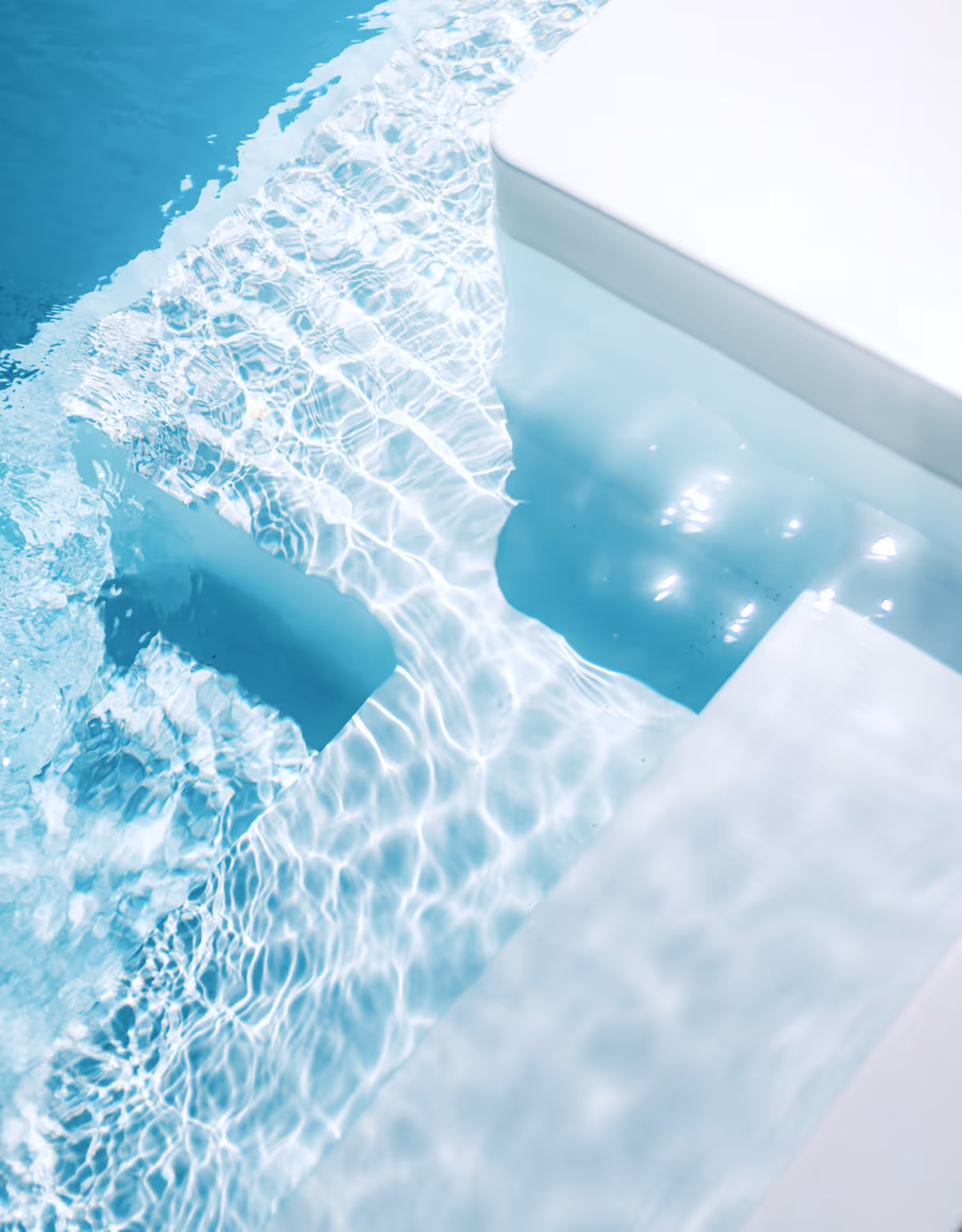 Clear blue pool steps submerged in water with sunlight reflections on the surface.