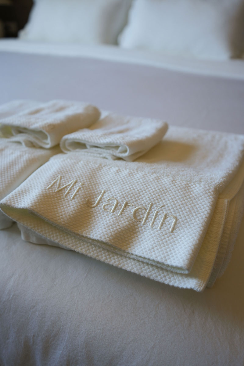 Toallas blancas dobladas sobre una cama con la palabra bordada Mi Jardín.
