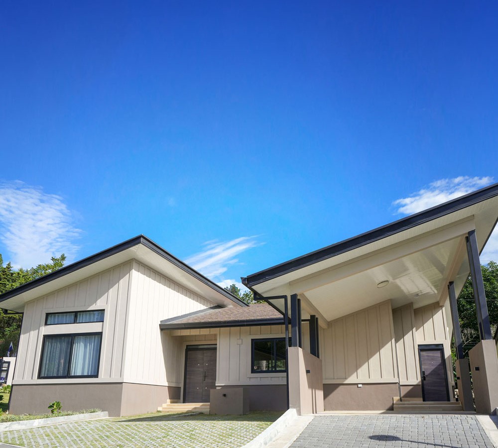 Casa moderna de un piso con techo inclinado, entrada principal y cochera cubierta bajo un cielo azul despejado.