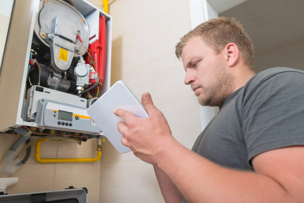Technician using a flashlight to inspect electrical wiring and components inside an open furnace