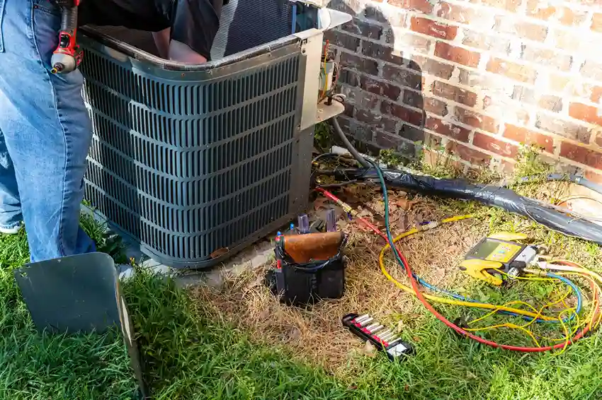 Technician’s leg next to an open AC unit with manifold gauges and tools laid out on the grass