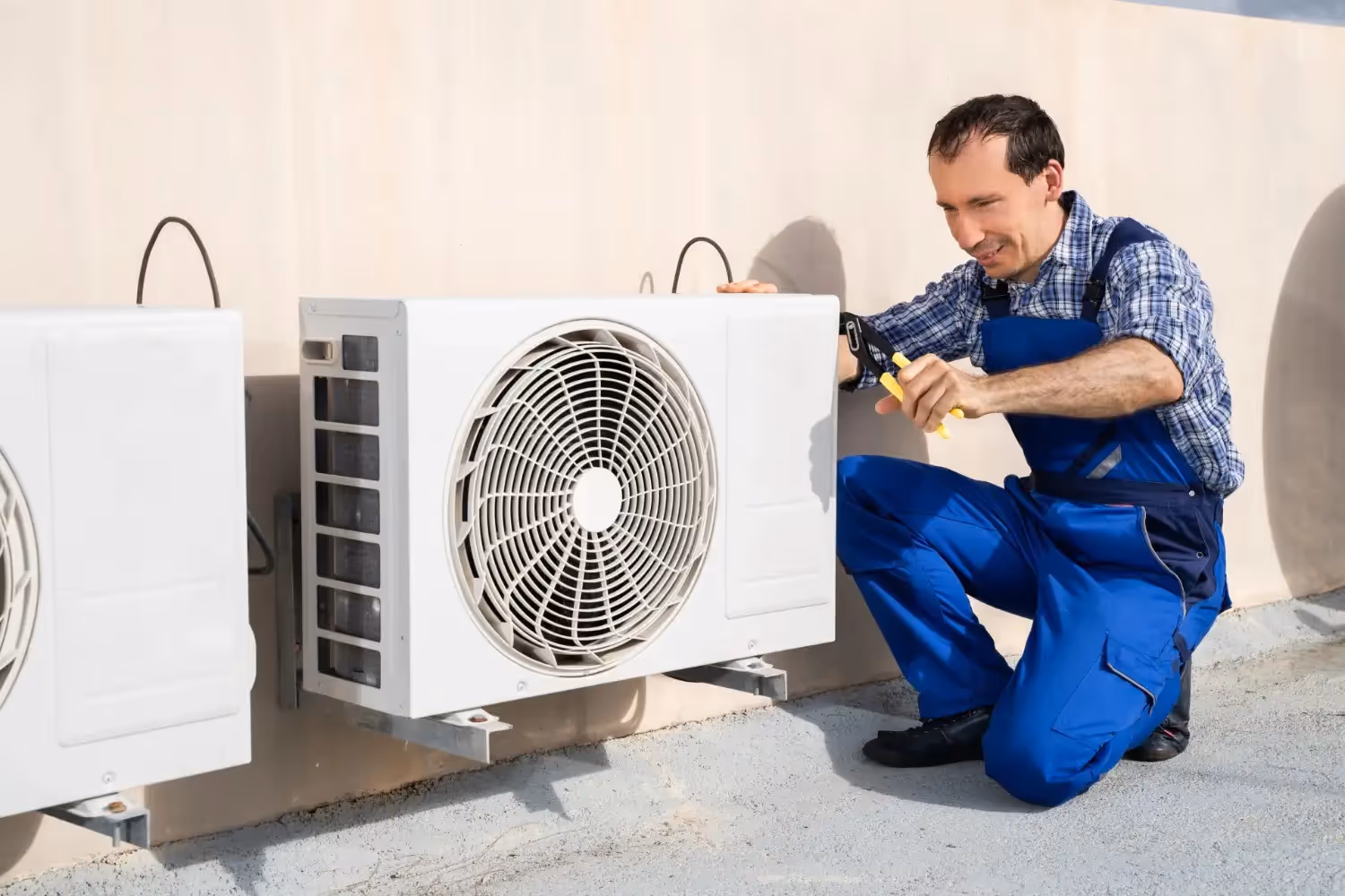 A smiling technician in blue coveralls works on a white mini-split unit on a rooftop