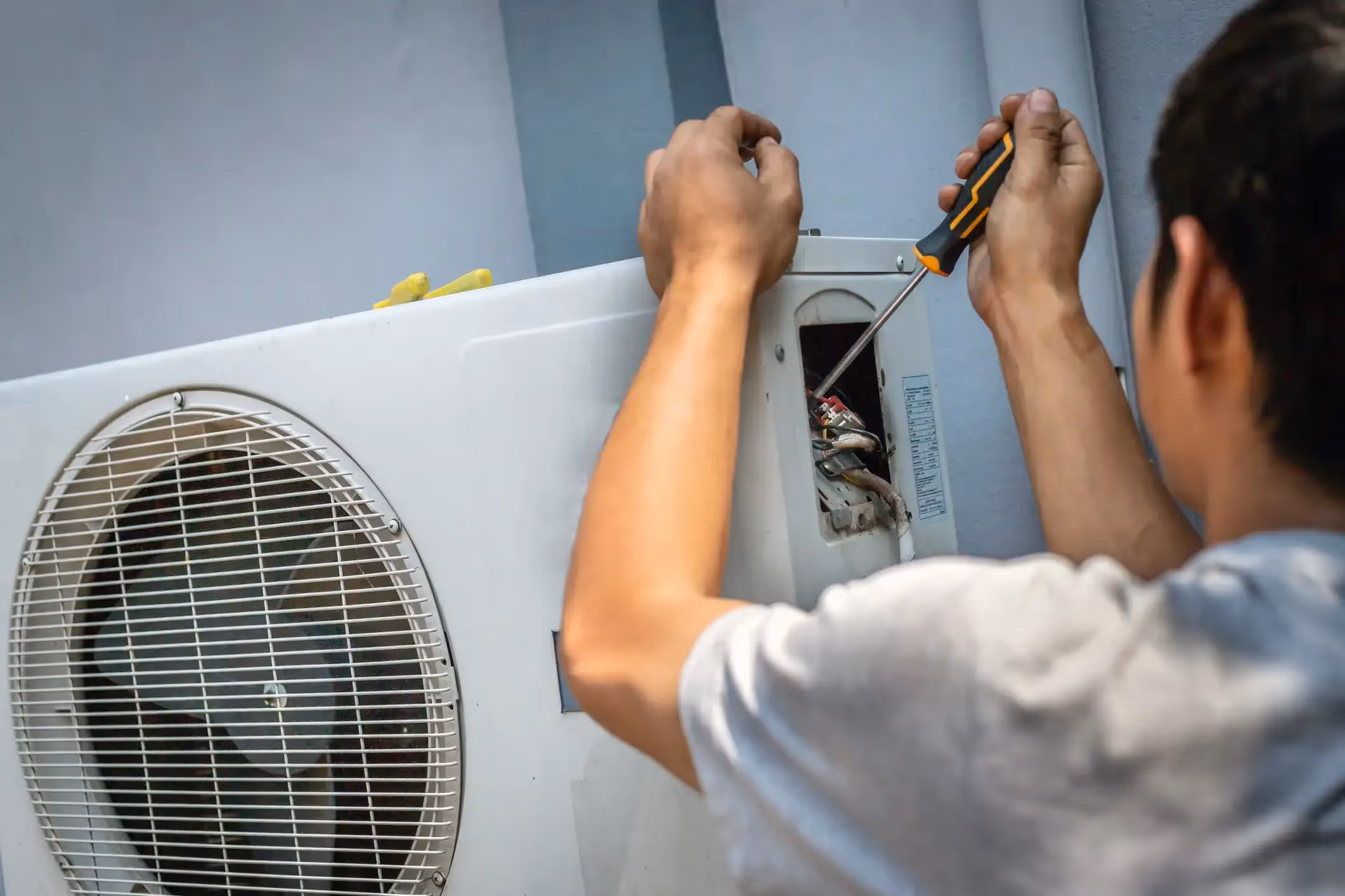 HVAC technician using a screwdriver to open and repair an outdoor AC condenser unit.