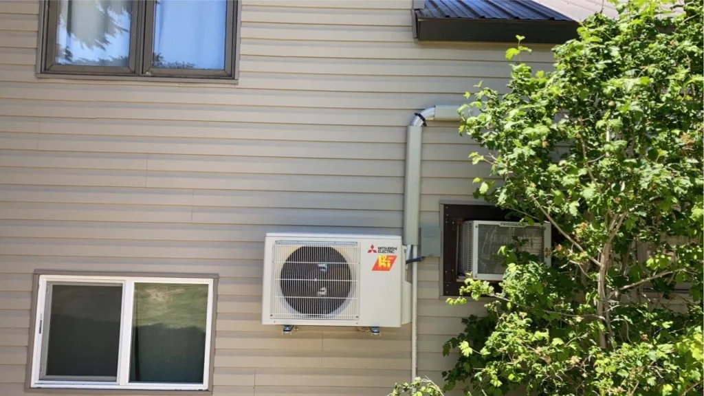 Air conditioning unit mounted on exterior wall of a home in Duchesne, UT, surrounded by greenery, illustrating professional HVAC services for efficient cooling maintenance.