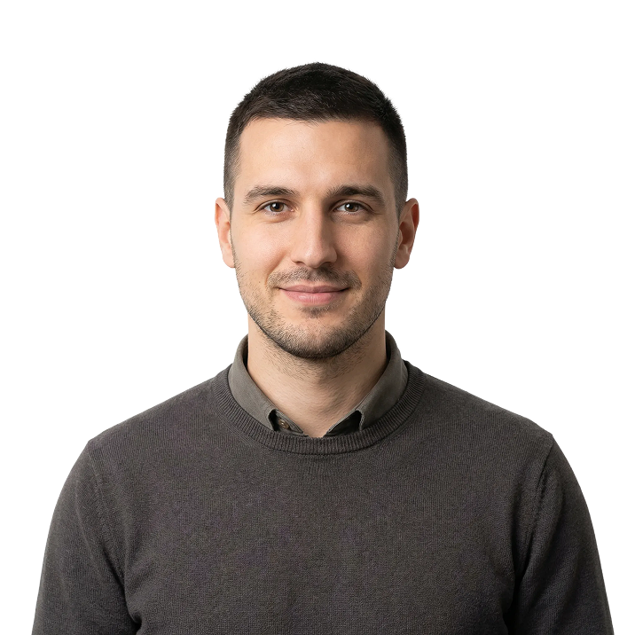 Smiling young man with short dark hair wearing a dark gray sweater over a collared shirt on a transparent background.