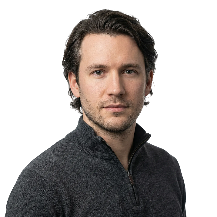 Portrait of a man with medium-length dark hair and light stubble wearing a dark gray zip-up sweater.