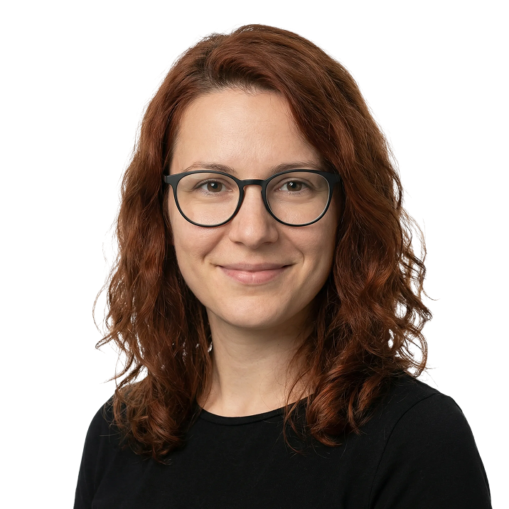 Smiling woman with curly red hair wearing black glasses and a black shirt, on a transparent background.