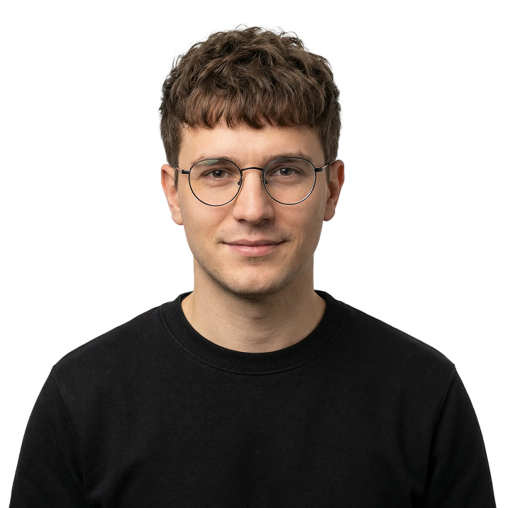 Young man with short curly brown hair wearing round glasses and a black crewneck sweater.