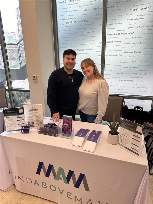 Jesse Cordova, Director of Business Development, and Ashley Ketchum, Director of Clinical Operations, representing Mind Above Matter, pose for a photograph at the 3rd Annual Resilience & Recovery Conference of Fort Worth. Jesse, on the left, is a person with light skin, wearing a dark suit jacket over a light shirt. Ashley, on the right, is a person with light skin, wearing a dark blazer over a light top. They are standing in front of a wall with a list of names and foundation logos, indicating sponsorship or support for the event. The text "Mind Above Matter" is visible at the bottom of the image, along with the conference name.