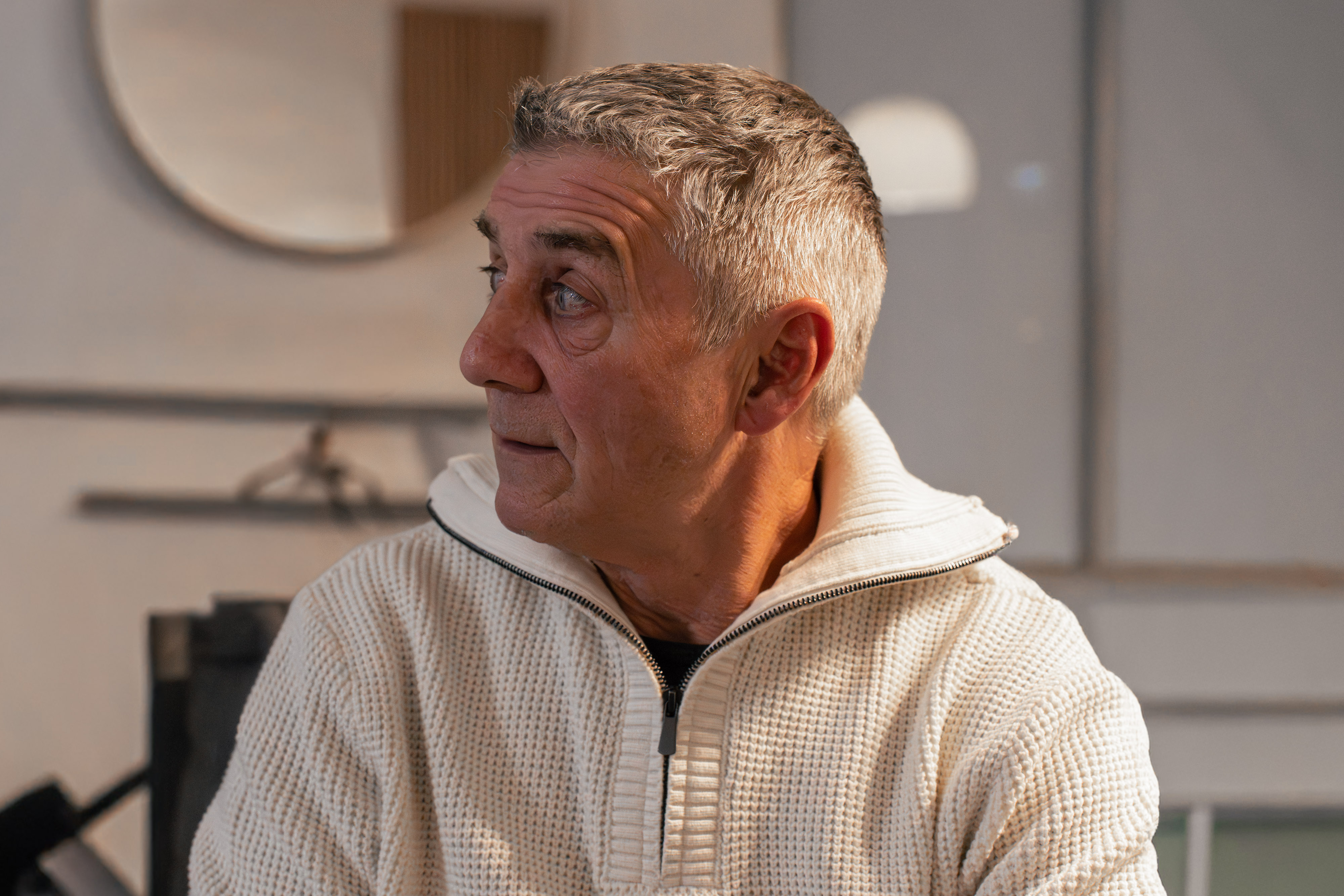 Homme âgé portant un pull blanc à col zippé regardant vers la gauche.
