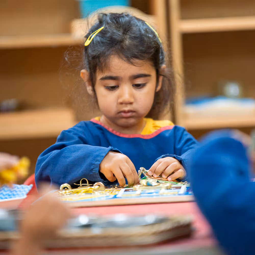 Young girl focused on manipulating small objects on a board in a classroom setting.