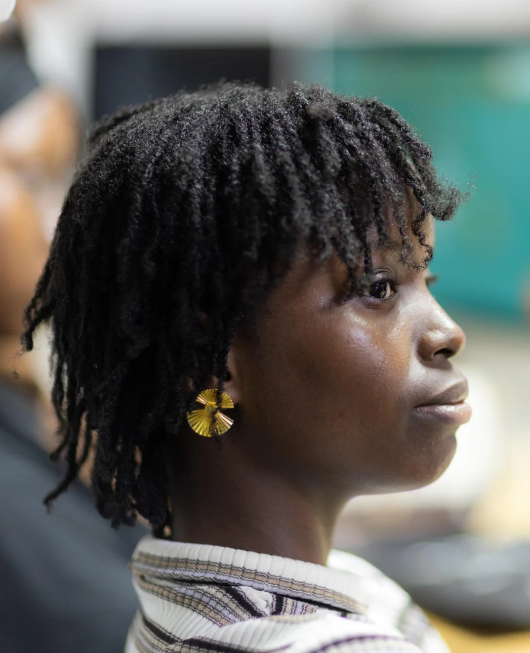 Profile of a young Black woman with short curly hair and a gold circular earring, wearing a striped top.