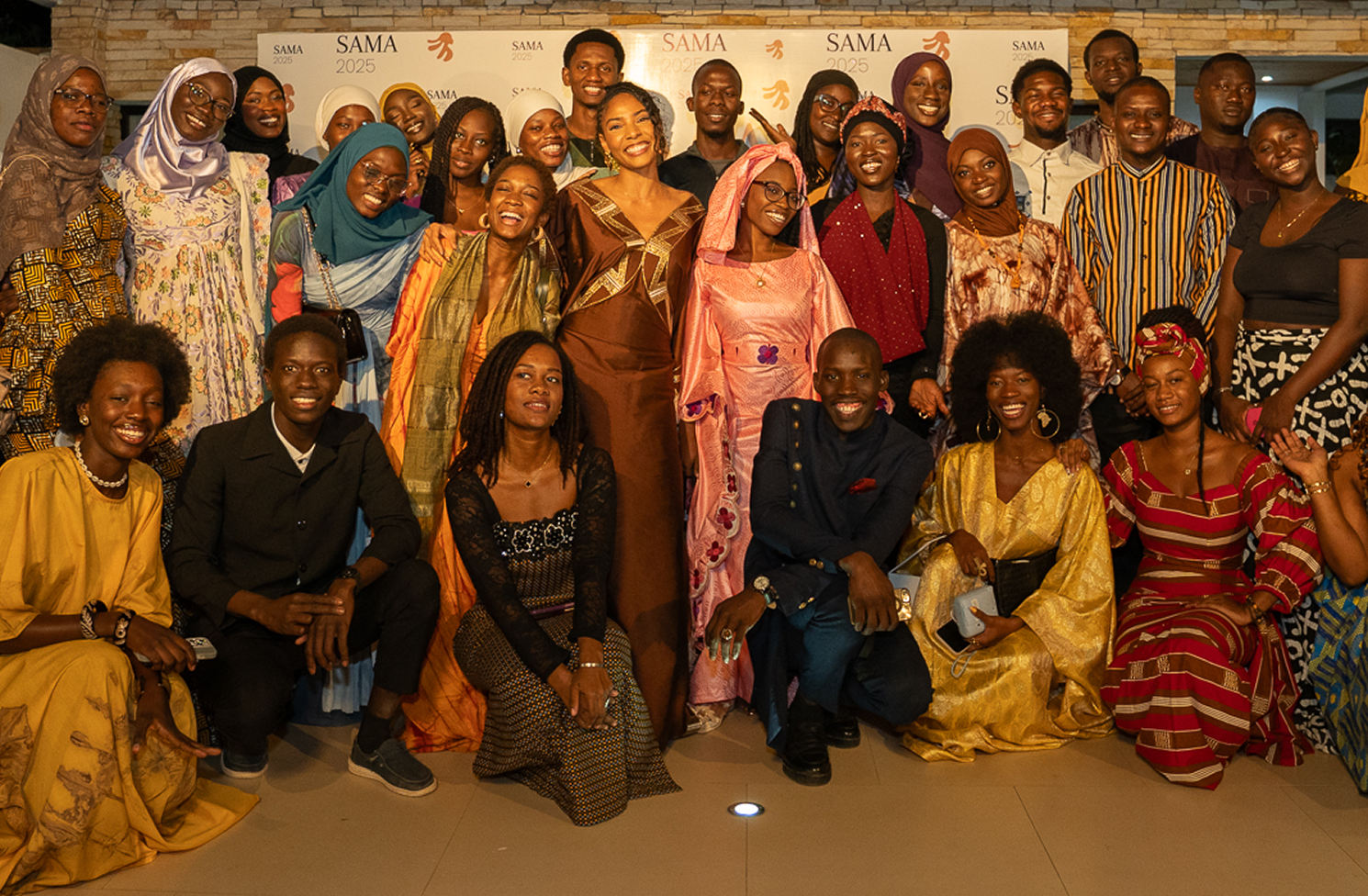Group of smiling young adults in colorful traditional and modern attire posing indoors in front of a SAMA 2025 banner.