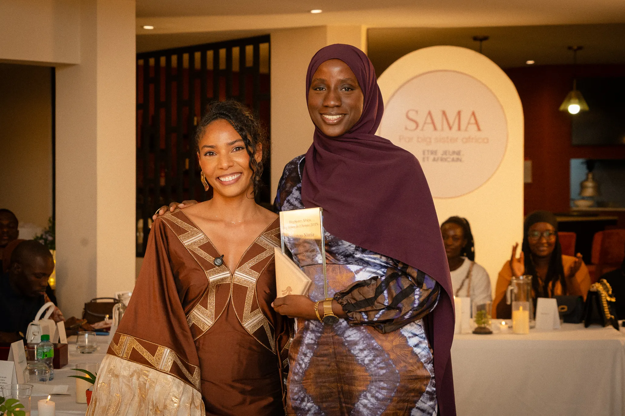 Photo of a phone screen showing a woman sitting on a yellow chair with a microphone in front, holding a phone, with camera settings visible around the image.