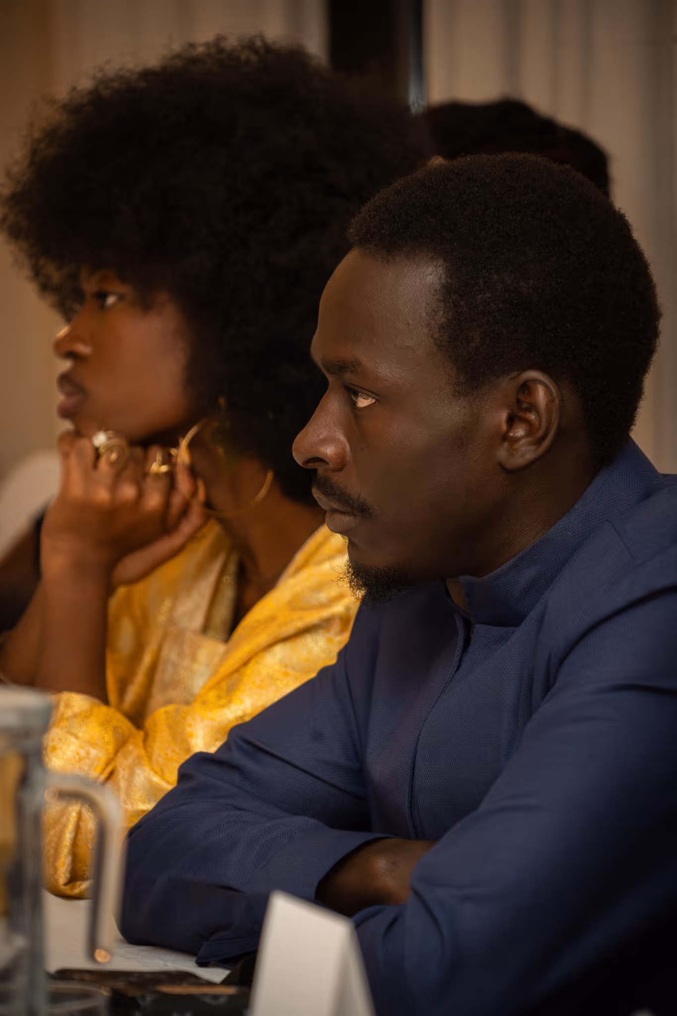 Photo of a phone screen showing a woman sitting on a yellow chair with a microphone in front, holding a phone, with camera settings visible around the image.