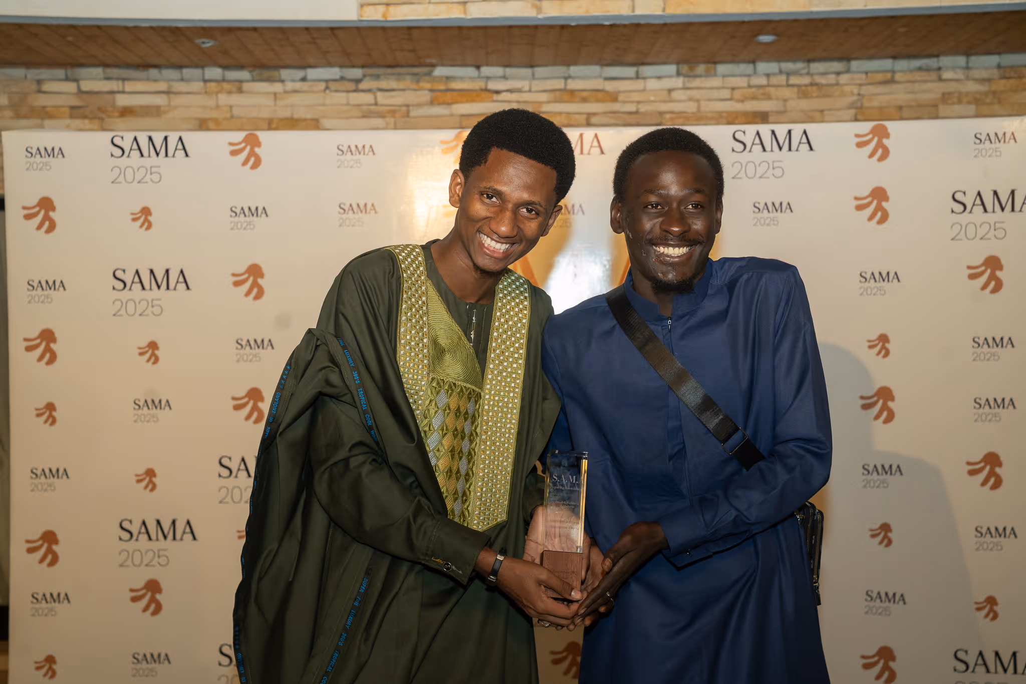 Two smiling men holding a trophy in front of a SAMA 2025 backdrop.
