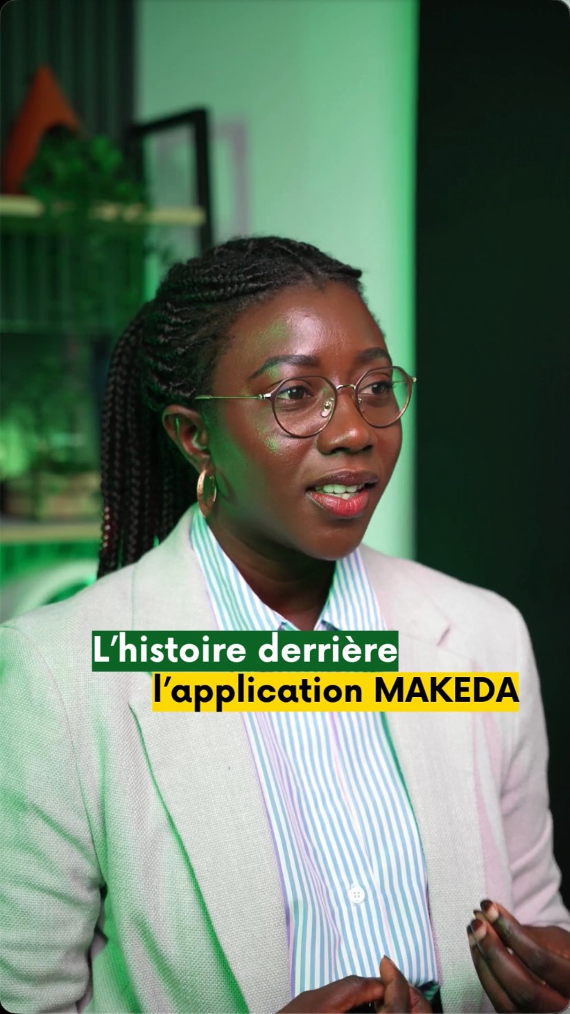 Woman with glasses and braided hair wearing a light blazer and striped shirt, speaking in a green-lit room with text overlay about the story behind the MAKEDA app.