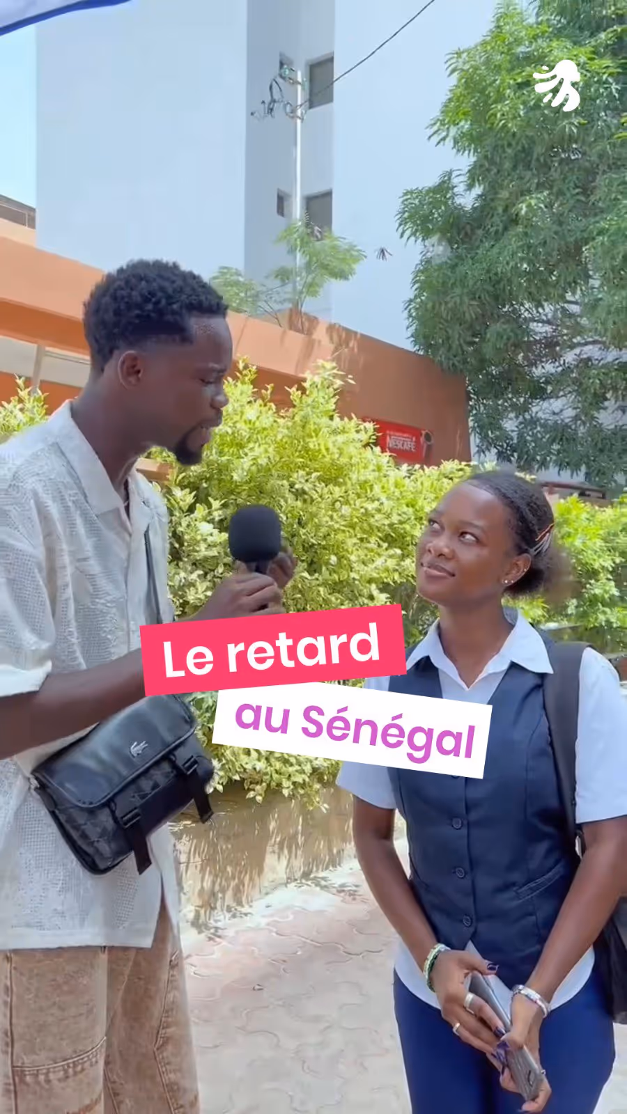 Man holding microphone interviewing a woman outdoors near green bushes in Senegal.