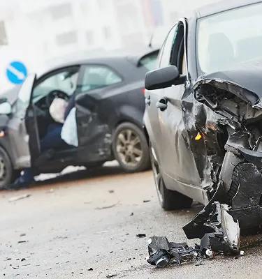 Two damaged cars on a road after a collision, with visible dents and broken parts on the front car.