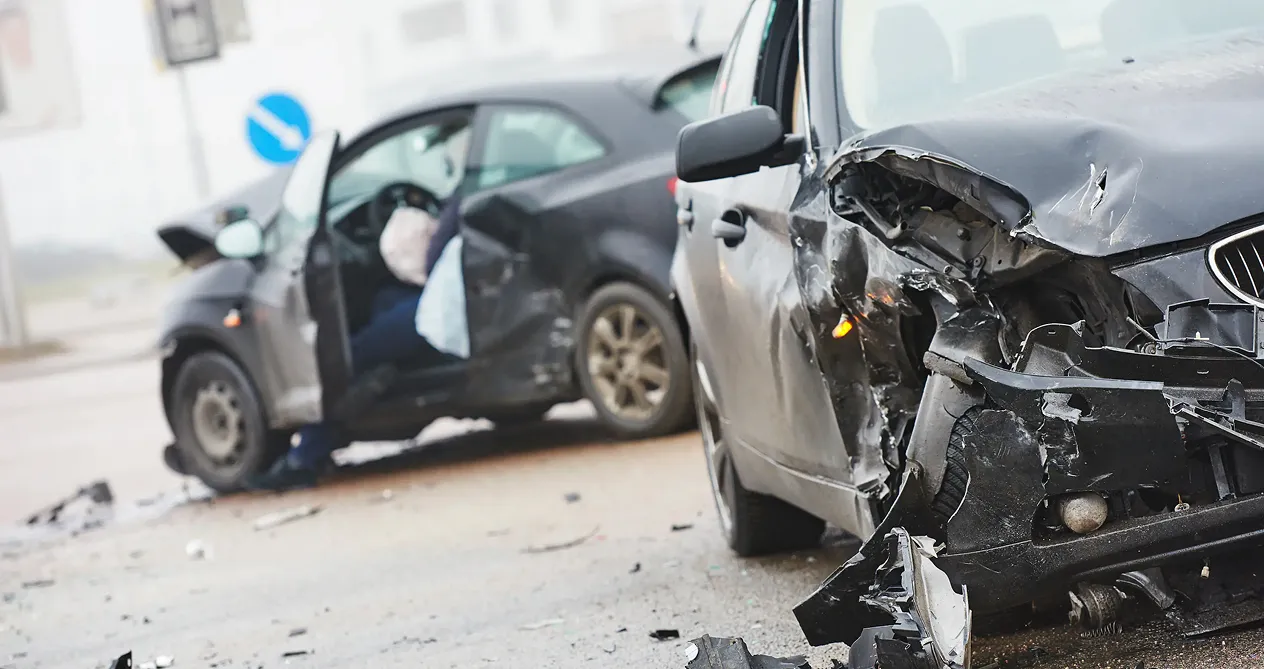 Two black cars with severe front and side damage involved in a crash, with airbags deployed and debris scattered on the ground.