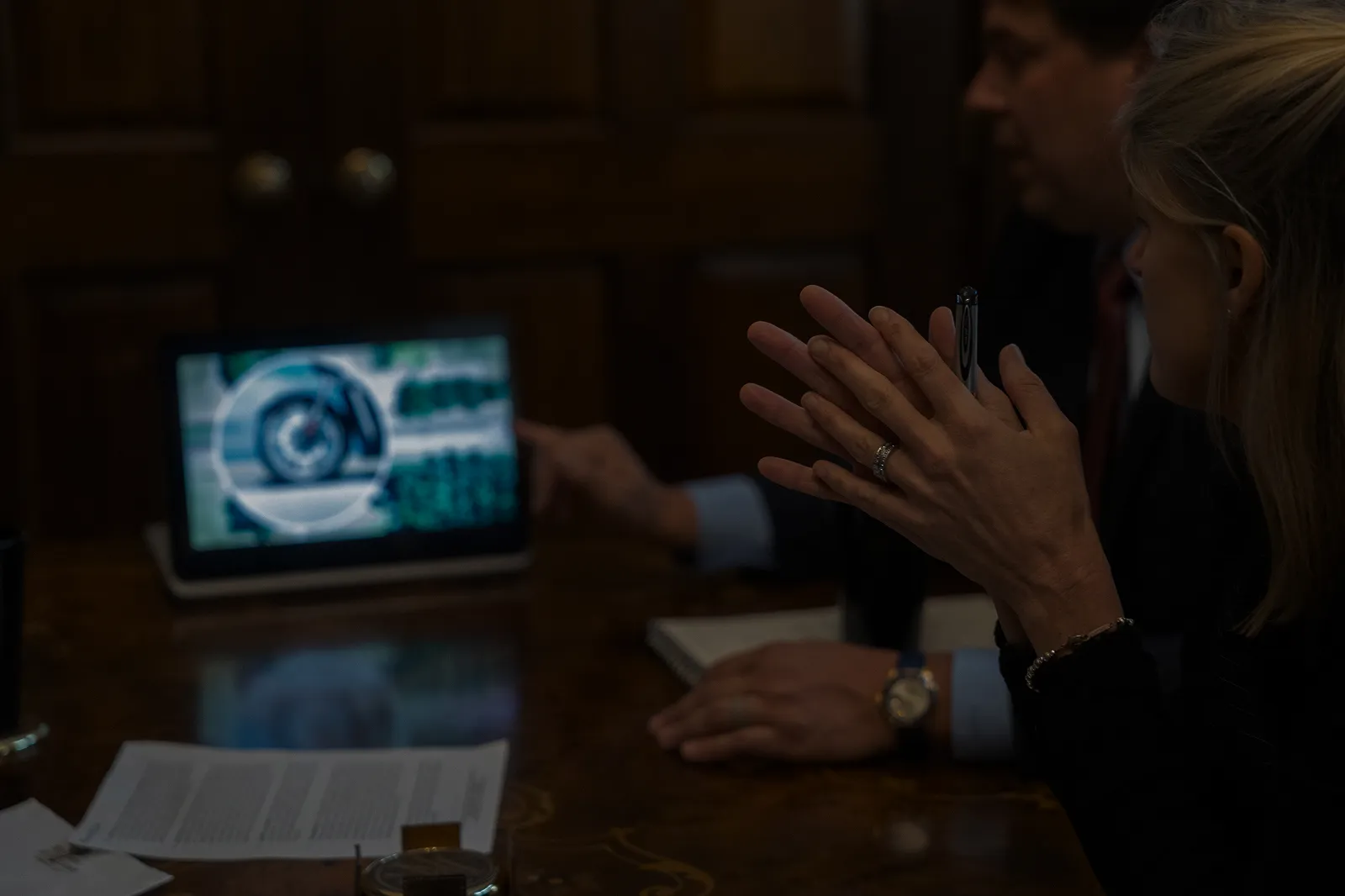 Two people in a dark room analyzing data on a tablet screen during a meeting.