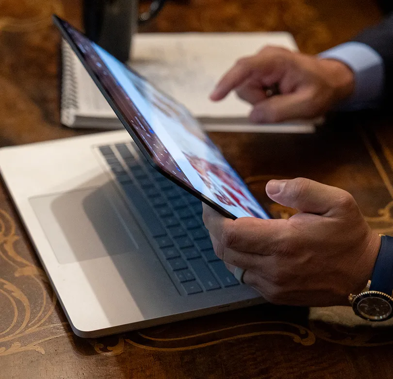 Person holding a tablet displaying medical images above an open laptop on a wooden table.