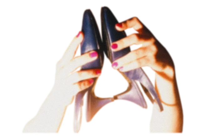 Hands with red nail polish holding a pair of black high-heeled shoes pointing upwards.