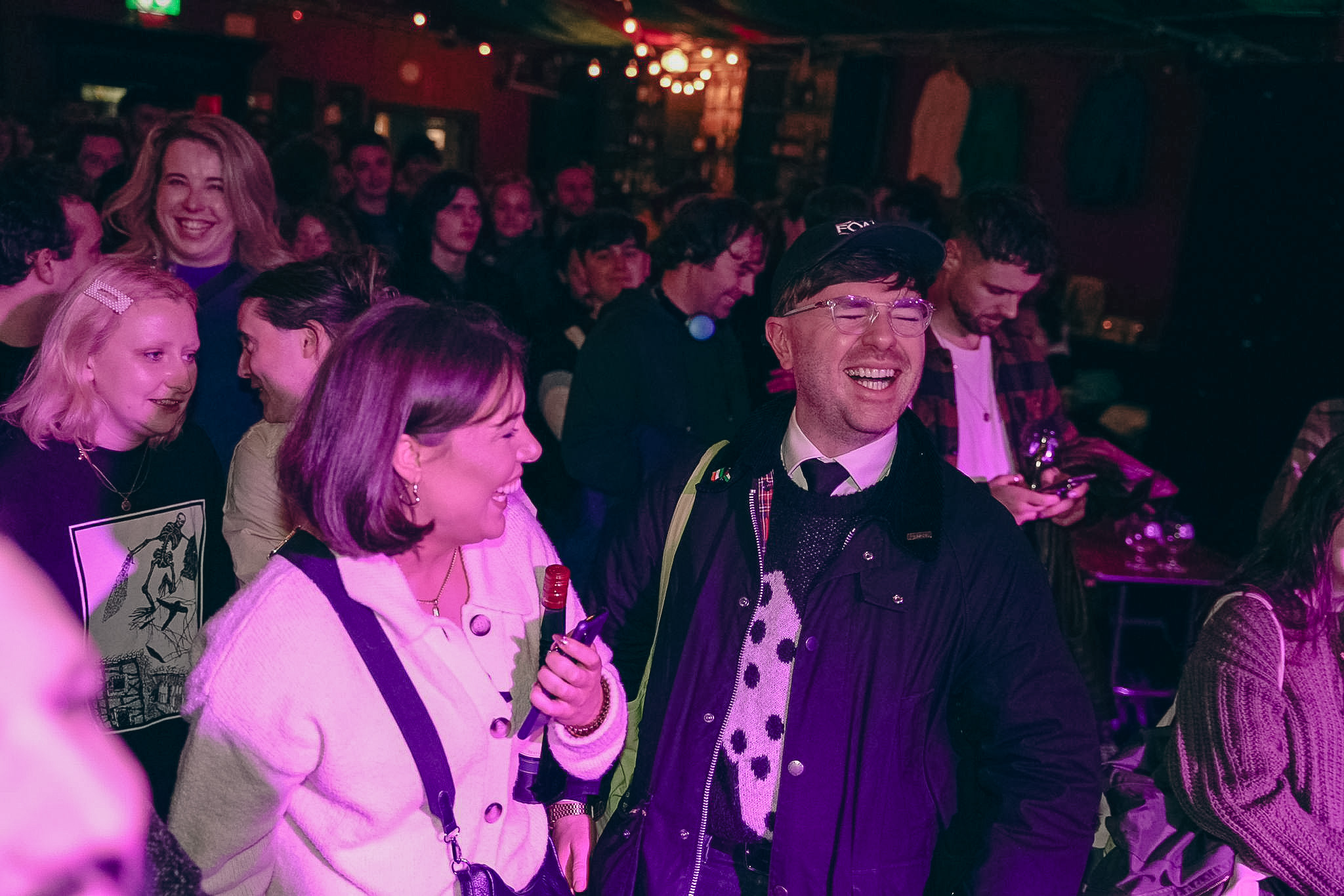 Group of people laughing and socializing at a crowded indoor event with dim lighting.