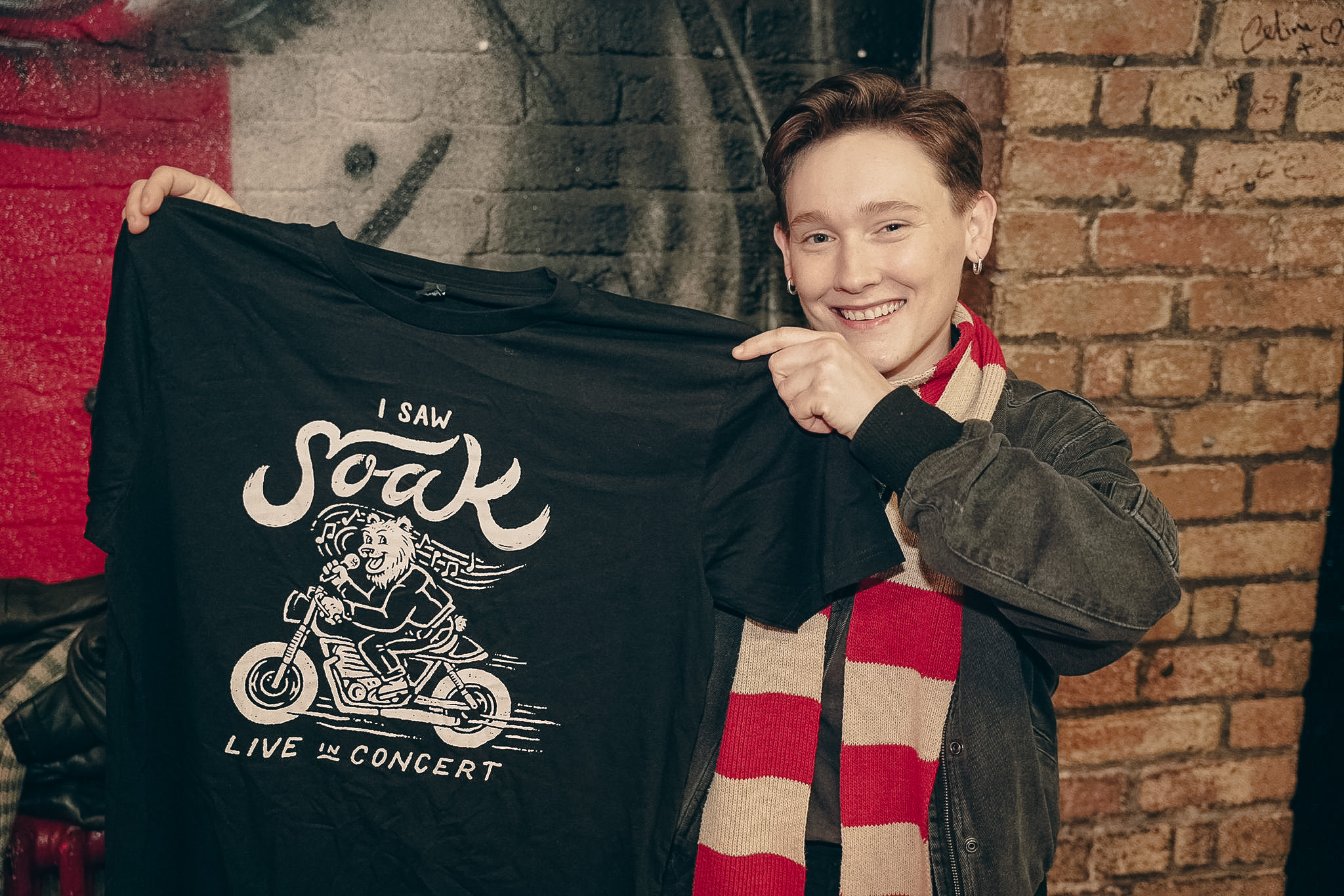 Smiling person holding a black T-shirt with a lion riding a motorcycle and the text 'I Saw Soak Live in Concert'.