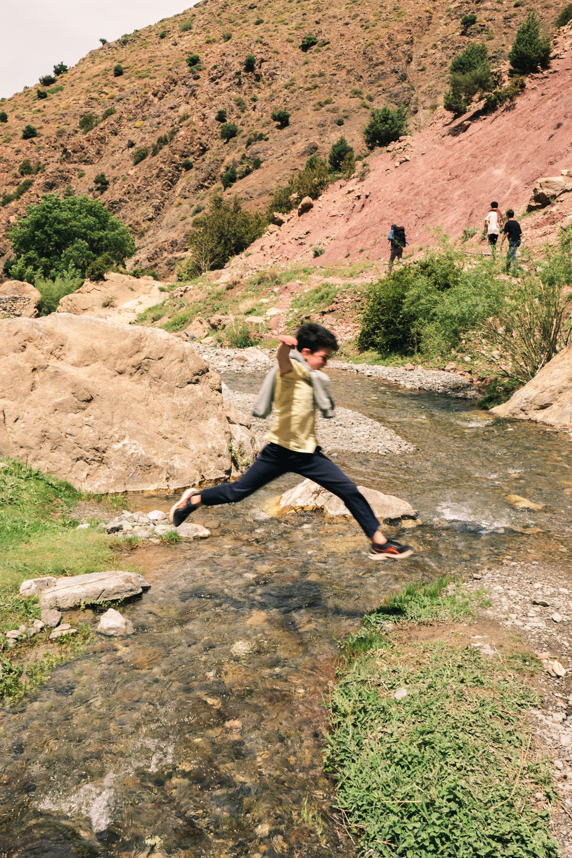 Enfant sautant par-dessus un ruisseau dans la vallée montagneuse du Haut Atlas, Maroc