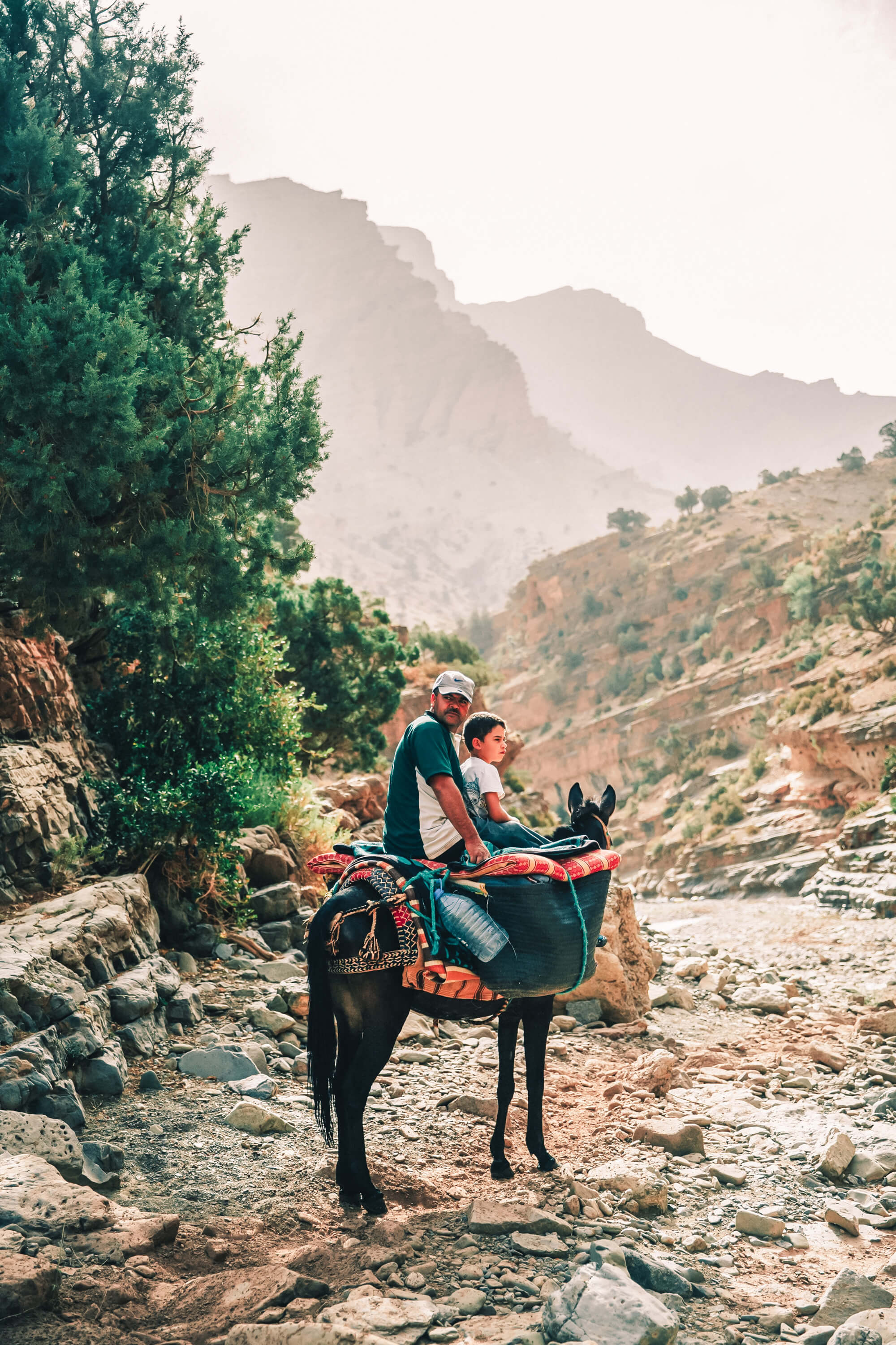Père et fils voyageant à dos d'âne dans la vallée rocheuse du Haut Atlas marocain